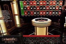 Das Bild zeigt den Moderator des Live Casino Spiels Lightning Roulette vor einer elektronischen Darstellung des Spielfelds, im Vordergrund befindet sich der Roulettekessel.