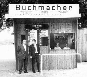 Ein Schwarzweißfoto der Unternehmensgründer Bernhard und Bernd Albers 1971, posierend vor ihrem Buchmacherstand. 