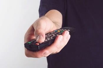 Eine Person hält eine TV-Fernbedienung in der Hand.